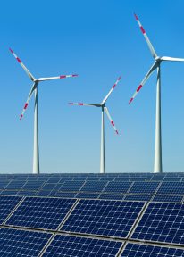 Windkrafträder und Solarmodule vor blauem Himmel.

Windmills and solar panels with a blue sky in the background.